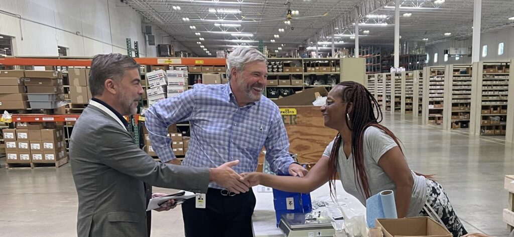 Representative Mike Carey visits Kimball Midwest. Image of 2 men and a woman in a large warehouse area, one man is shaking the woman's hand. They are all smiling.